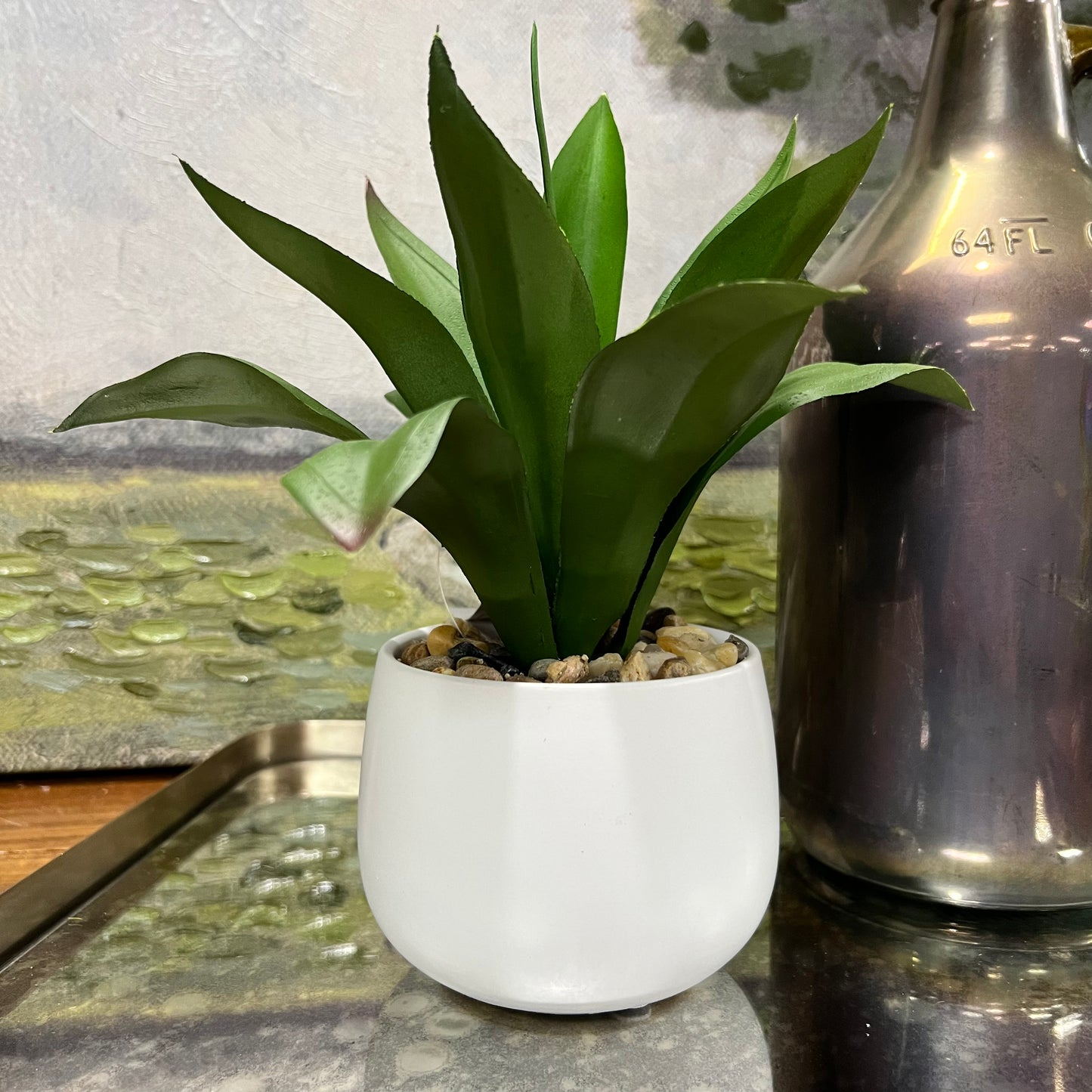 faux light green plant in white pot on a table next to a vase.