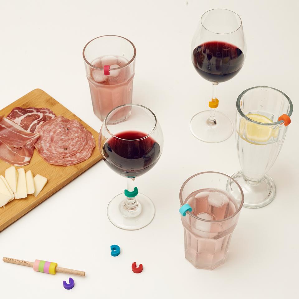 multiple wine glasses displayed with rainbow wine markers next to a charcuterie on a white background