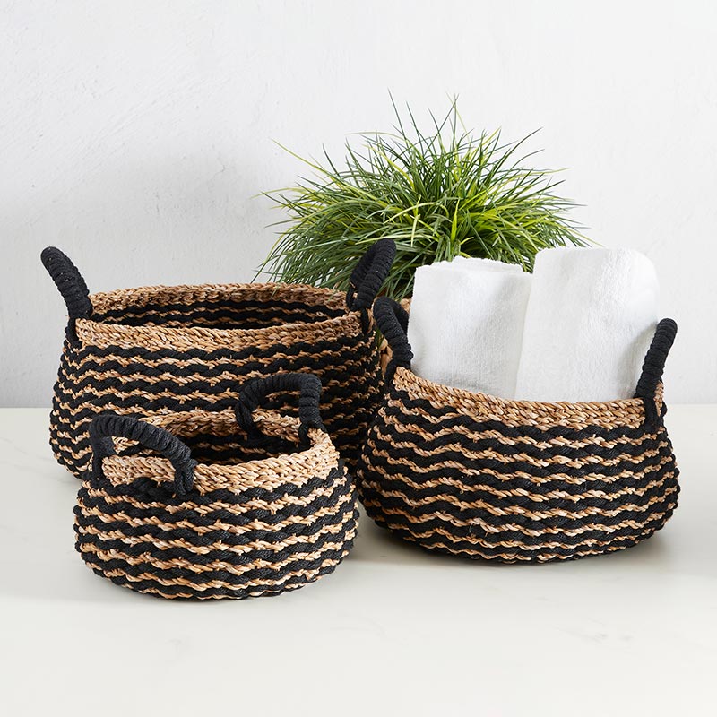 small, medium, and large black and natural baskets with handles. medium basket has rolled towels in it.