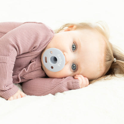 a little girl laying on her side with the darling bubbi pacifier in her mouth