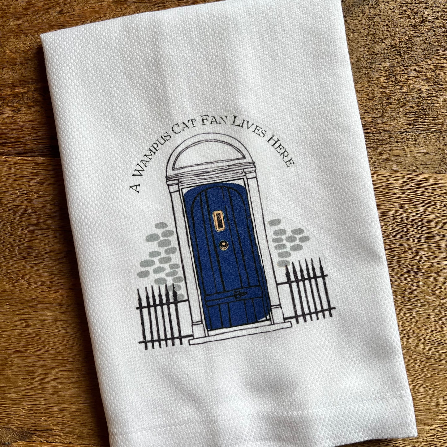 white towel with blue front door design and "a wampus cat fan lives here" across the top.