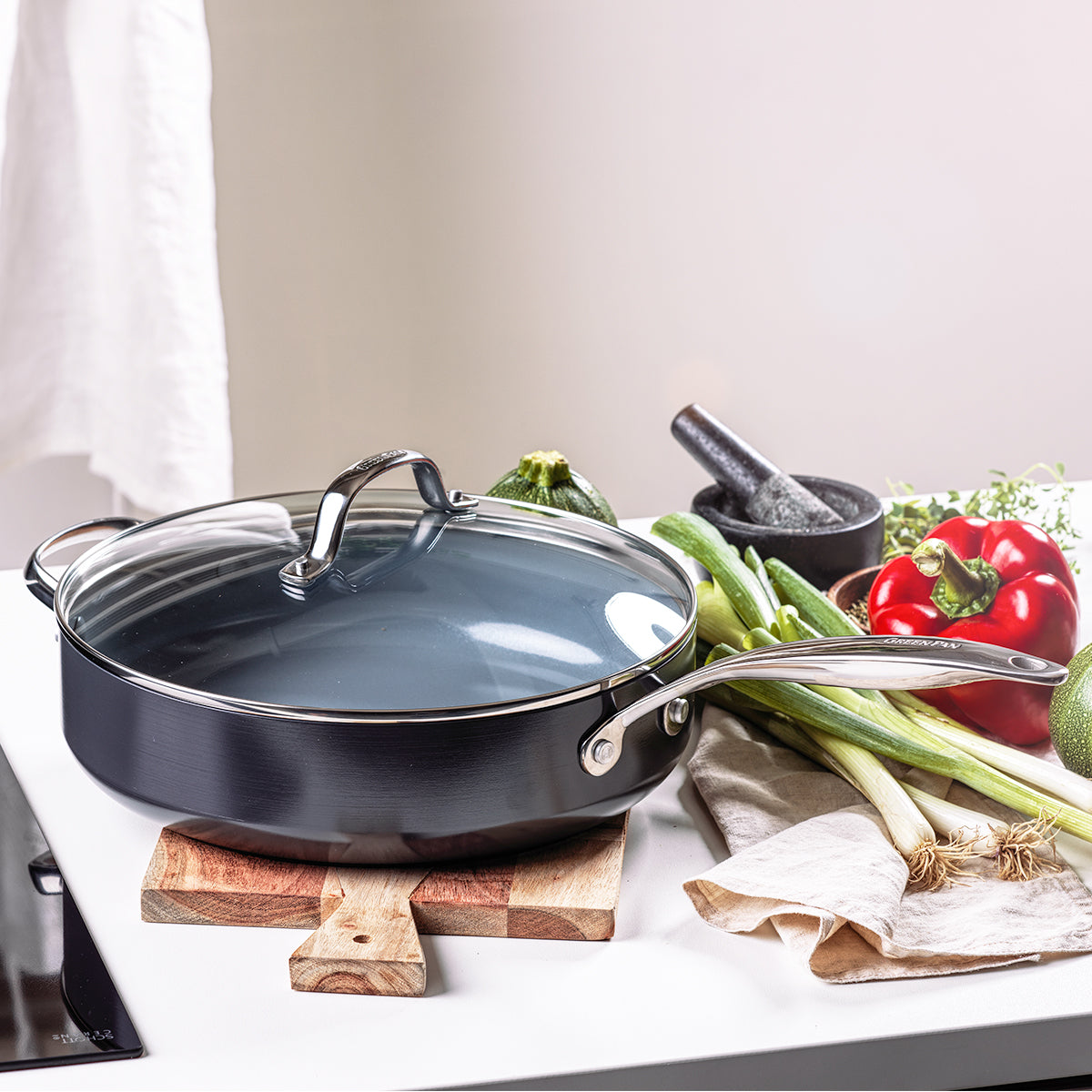 saute pan on cutting board with veggies and mortar and pestle next to it on kitchen countertop.