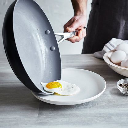 fried egg sliding out of fry pan onto plate on wooden countertop.