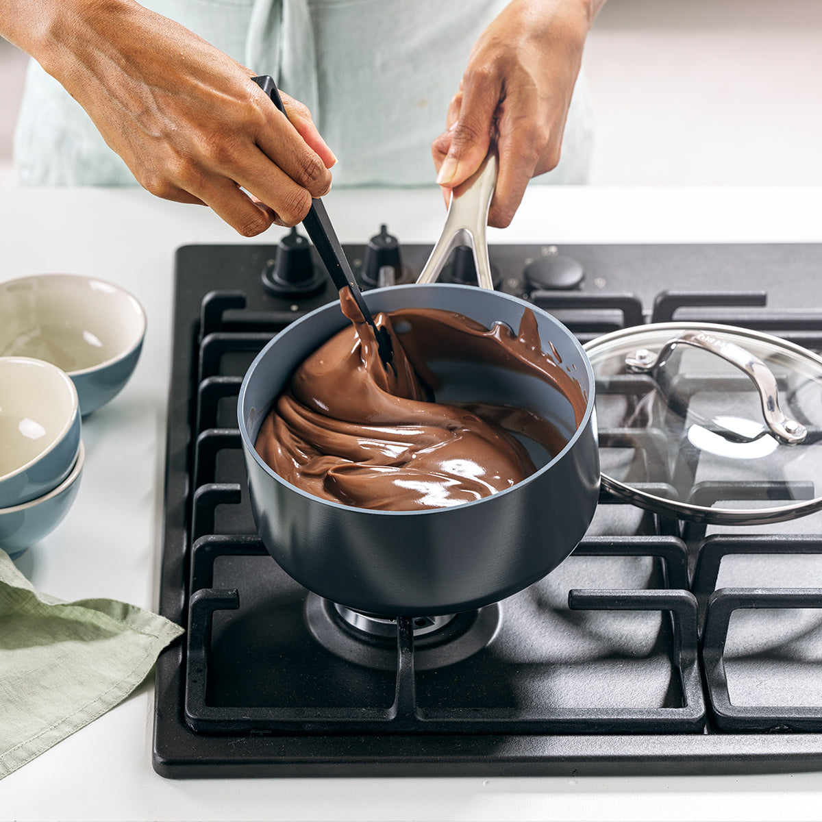 sauce pan on stove top with hands stirring chocolate sauce in it.