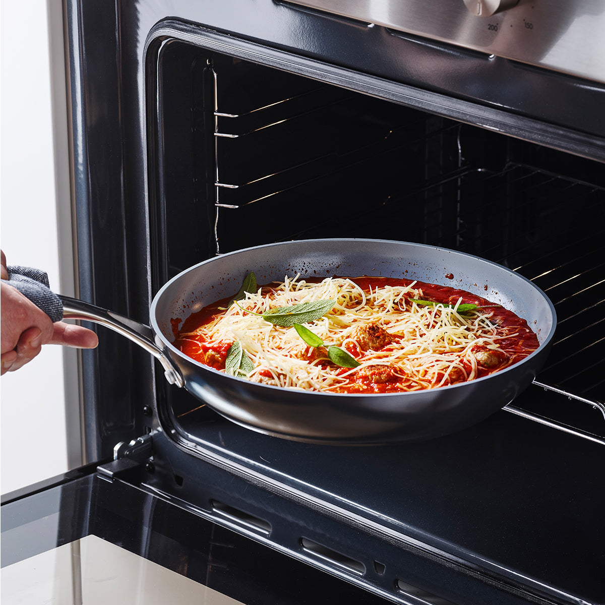 hands putting fry pan filled with pasta onto oven.