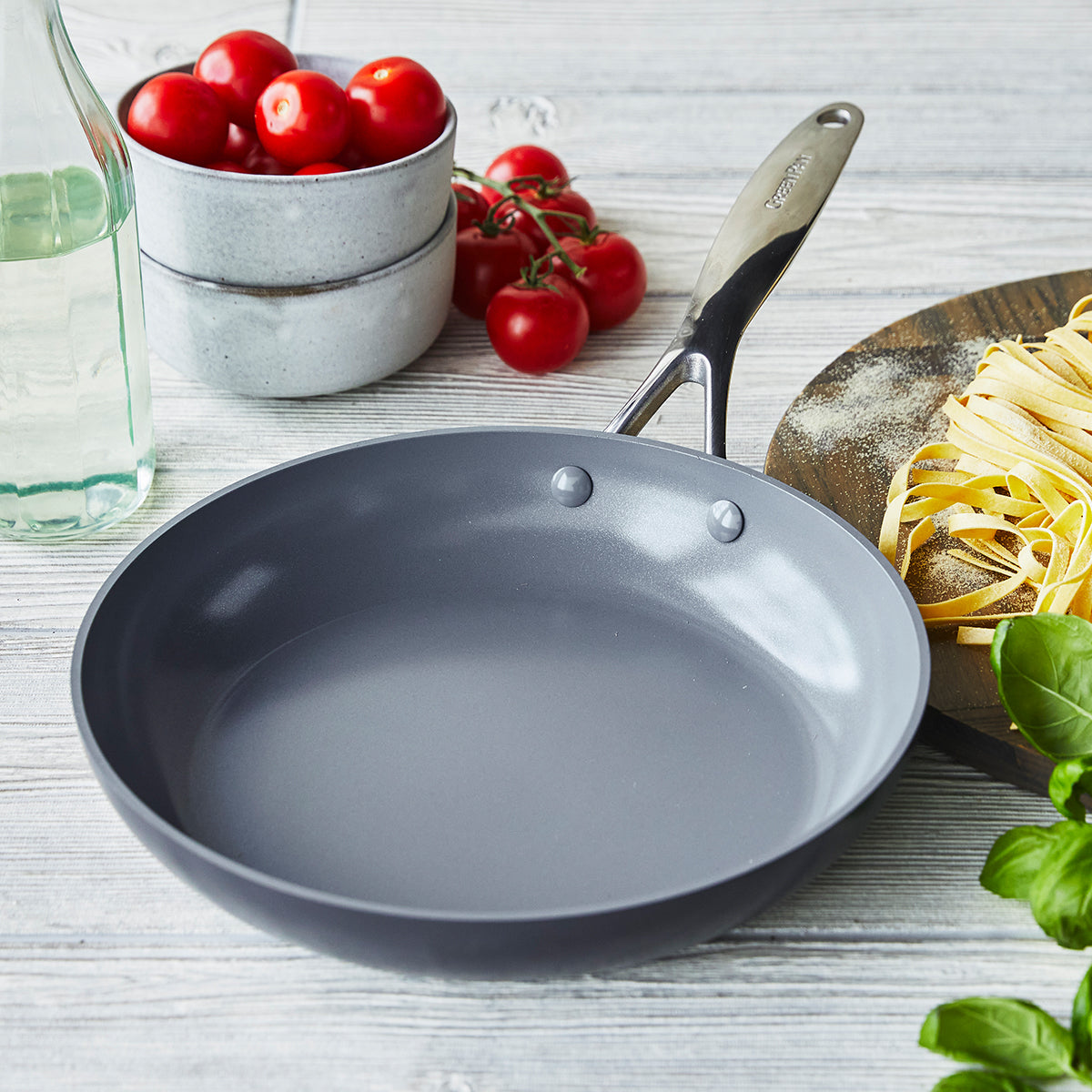 fry pan on countertop surrounded by tomatoes, pasta, and herbs.