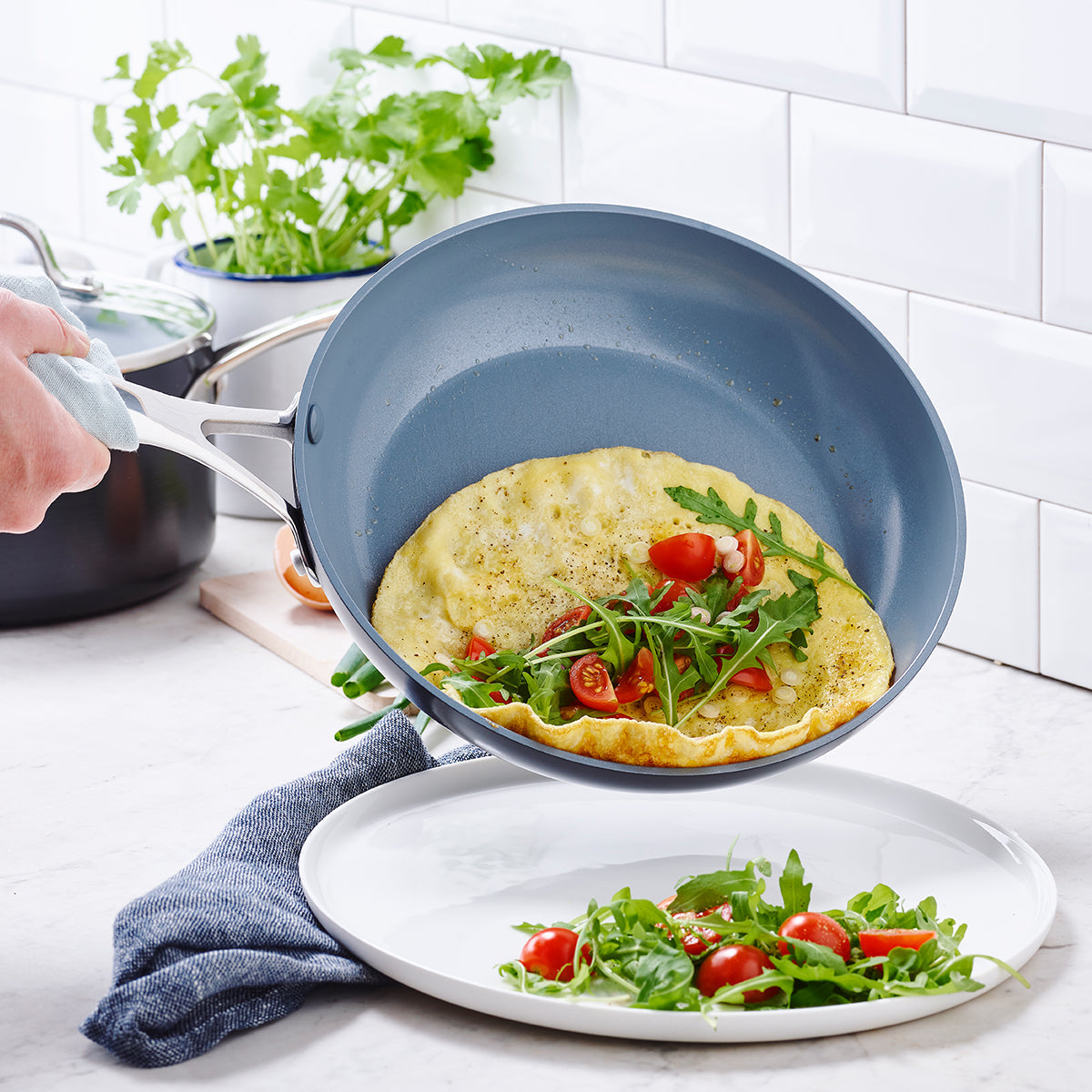 omelet sliding out of fry pan on to plate with greens and tomatoes on it.