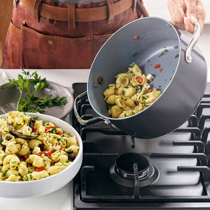 a person pouring a cooked pasta dish out of the valencia pro nonstick stockpot next to the stovetop