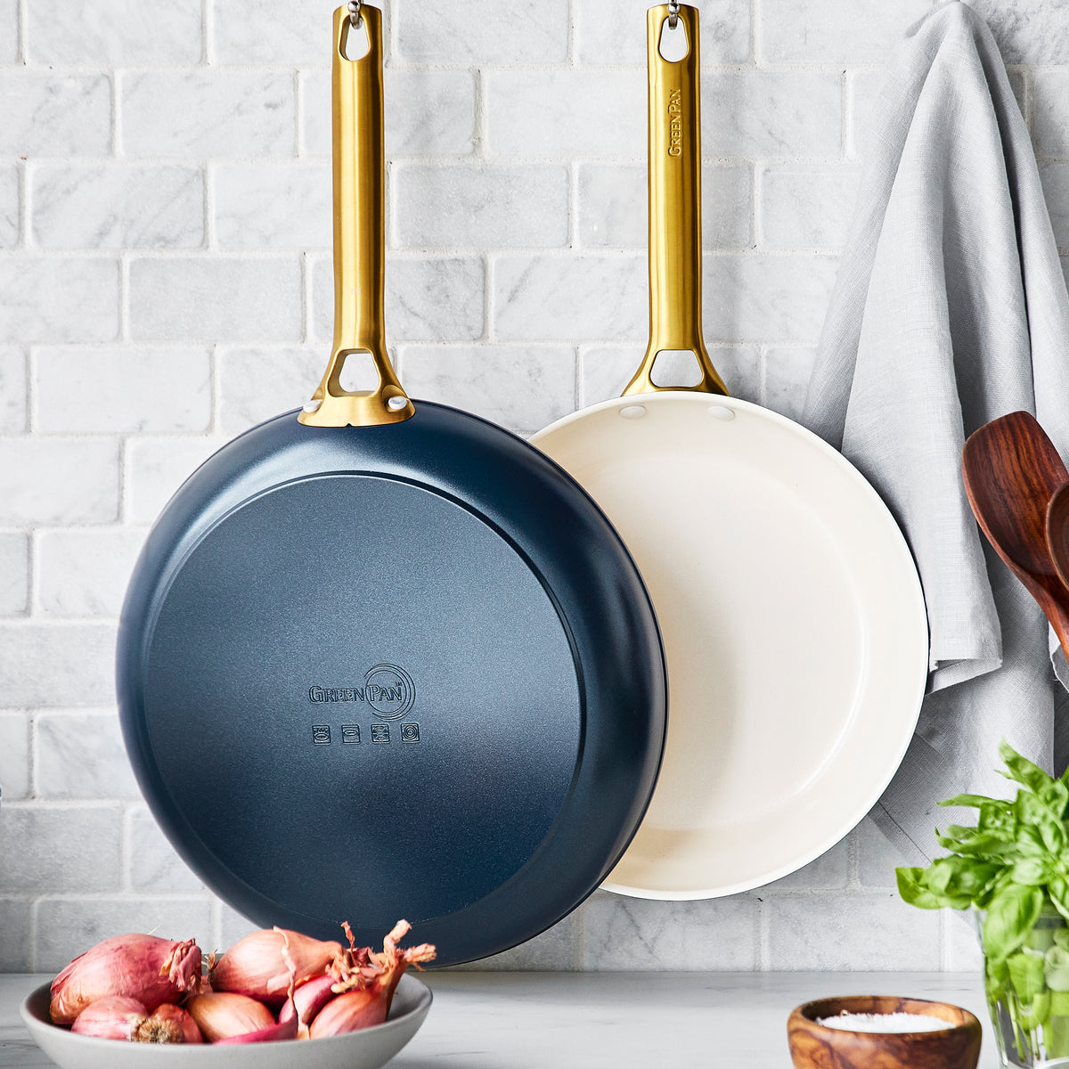 large and small navy fry pans hanging in front of grey tile backsplash.