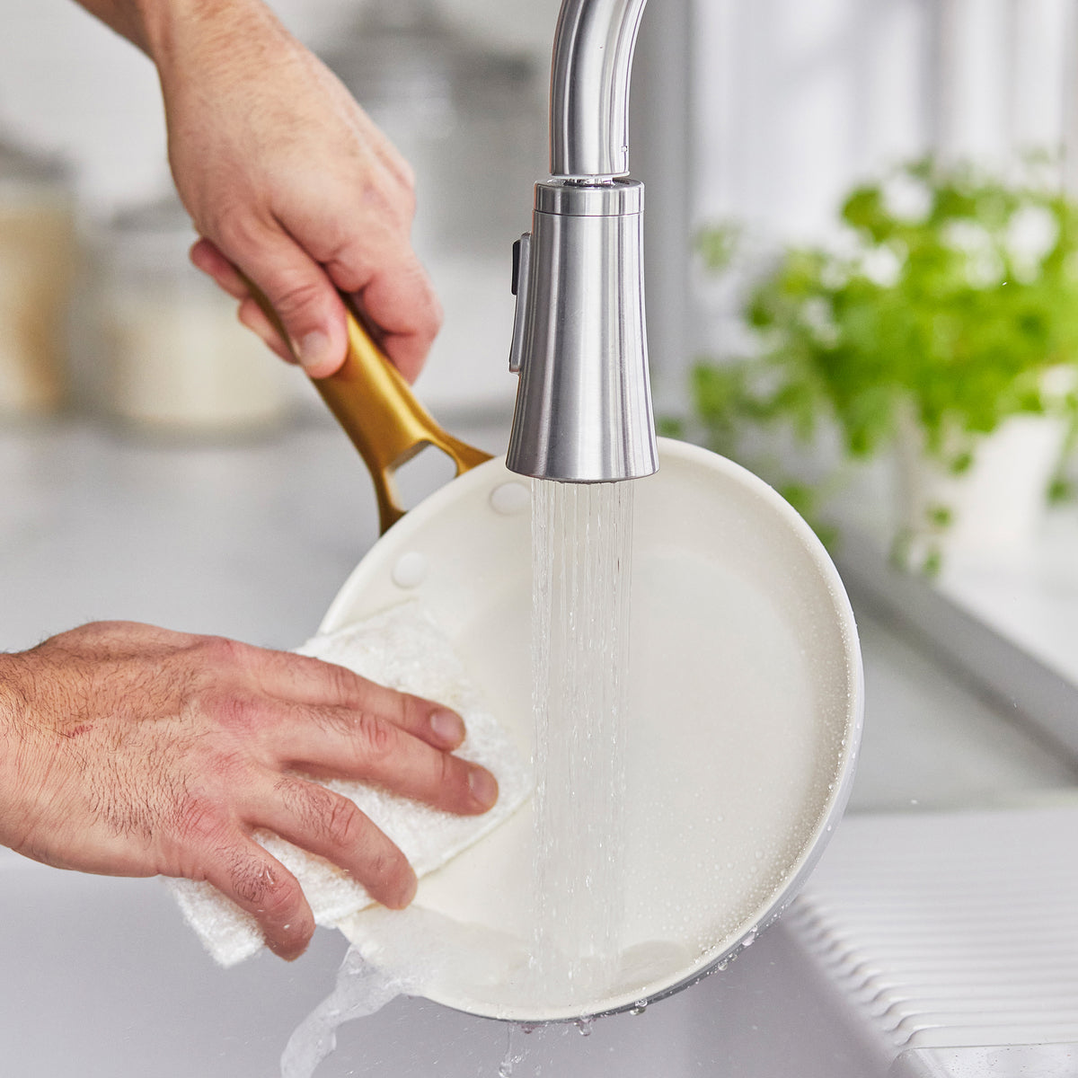 hands washing fry pan with sponge over sink.