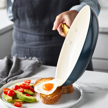 fried egg sliding out of fry pan onto plate with toast, avocado, and tomatoes.