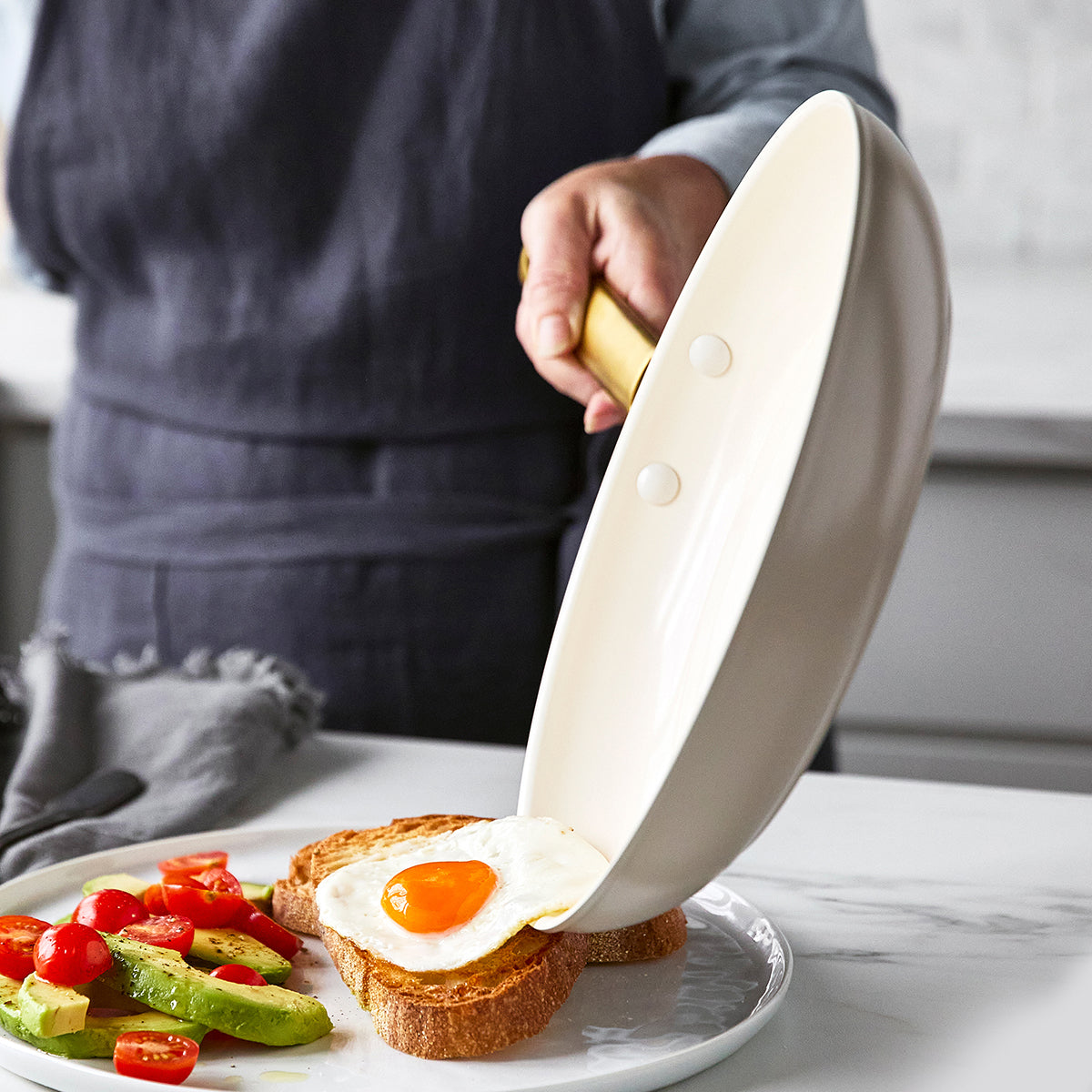person sliding fried egg out of fry pan on the plate with toast, avocados and tomatoes.
