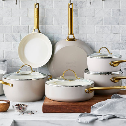 taupe cookware arranged on marble countertop with grey tile backsplash.