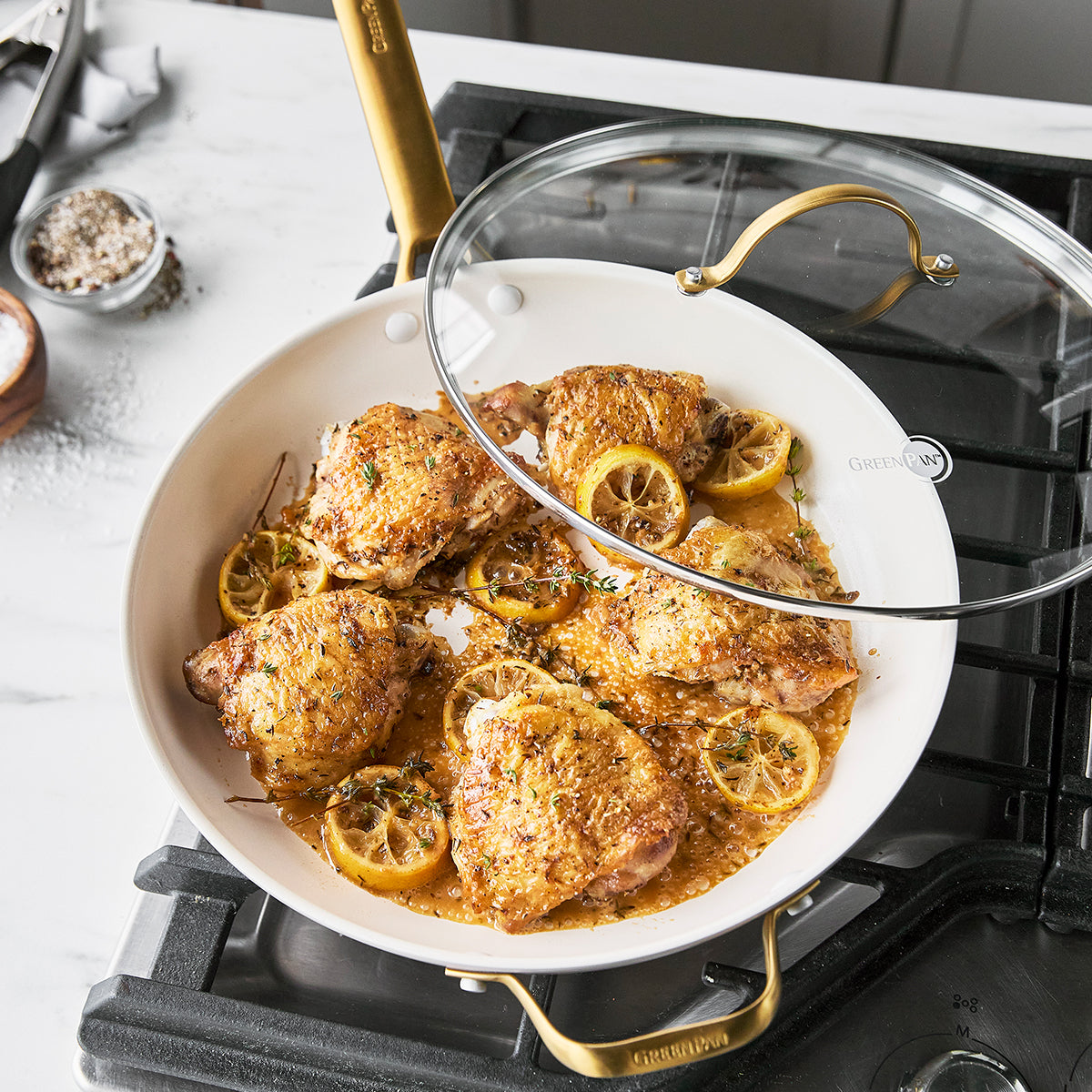 fry pan on stovetop with chicken and lemon inside.