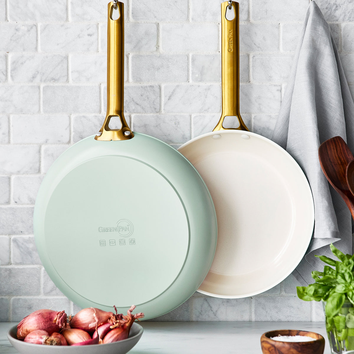 large and small mint green fry pans hanging in front of grey tile backsplash.