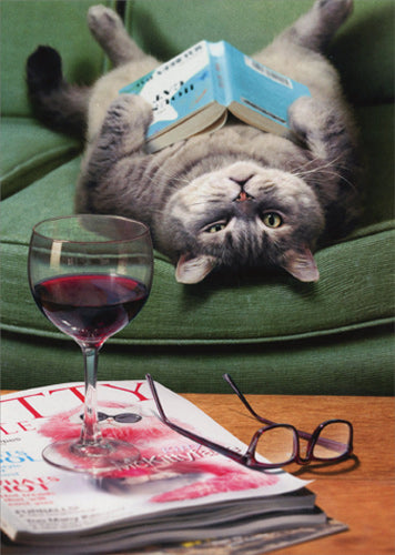 front of card has a fat gray cat laying on its back with a book on its belly, a glass of wine, reading glasses, and magazines on a coffee table
