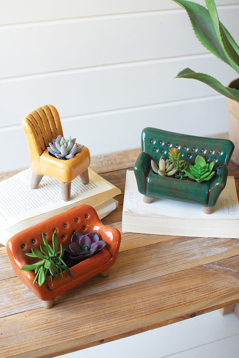 all three colors and styles of ceramic planters filled with small succulents and displayed on top of books next to a large plant on a wooden surface