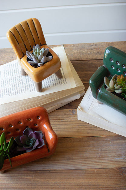 top view of the ceramic chair and sofas filled with small succulents and displayed on top of books on a wooden surface