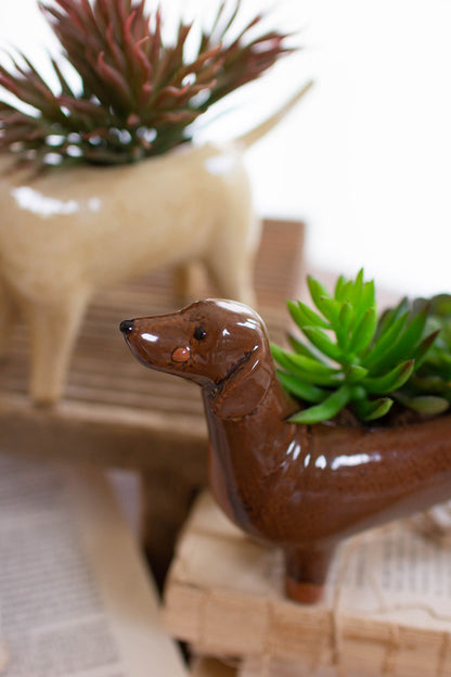 close up view of the dachshund ceramic dog planter displayed on a stack of books with another dog planter in the background against a white wall 