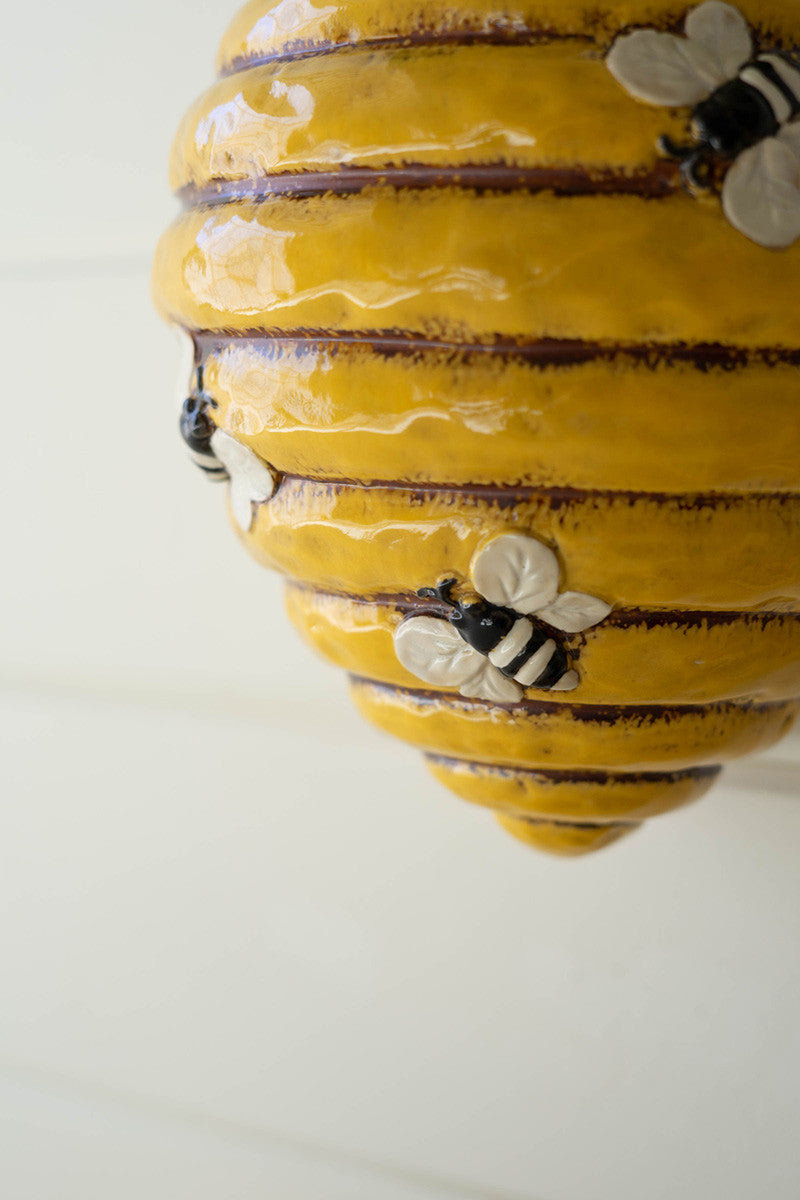 close up view of the ceramic bee hive wall planter hanging on a white wood slat wall