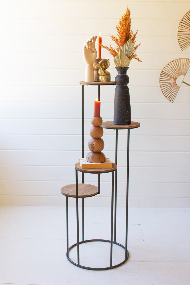 four tiered wood and metal stand displayed with wood vase wooden candle stick and decor against a pale pink background