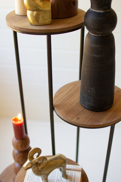 close up view of the four tiered wood and metal stand displayed with wooden vase wooden candlestick and decor against a pale pink background