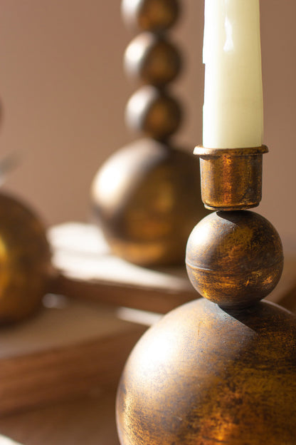 close up view of all three sizes of antique brass taper candle holder displayed with burning candles next to a succulent displayed on books against a taupe background