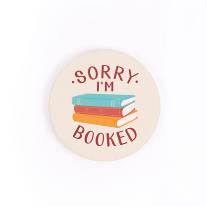 sorry i'm booked car coaster is cream with a stack of three different colored books and text in red displayed on a white background