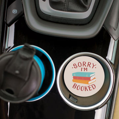 top view of the sorry i'm booked car coaster displayed in the cup holder in a car
