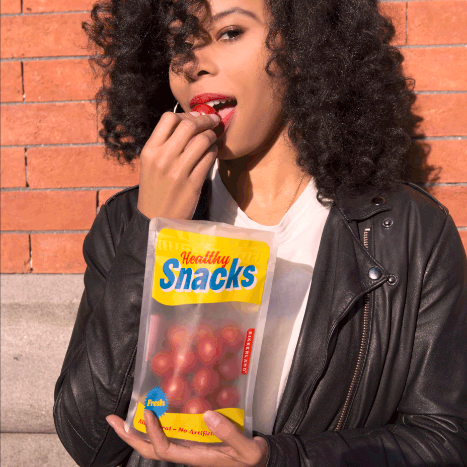 a woman eating cherry tomatoes out of the medium snack zipper bag against a brick building