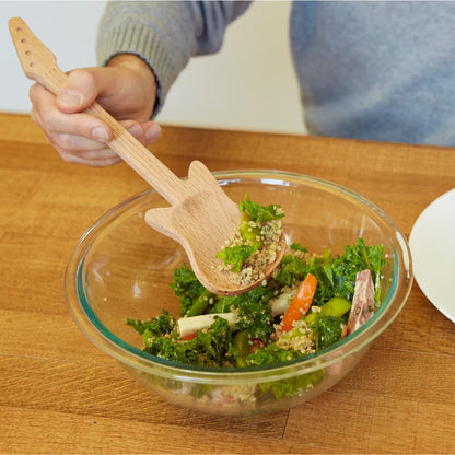a person mixing a bowl of salad with the rockin wooden kitchen serving spoon on a wooden surface