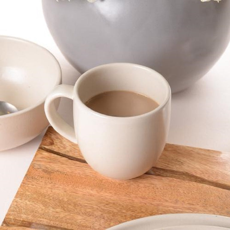 pacifiaca vanilla mug filled with coffee and displayed on a wood board next to a bowl plate and gray vase on a white surface