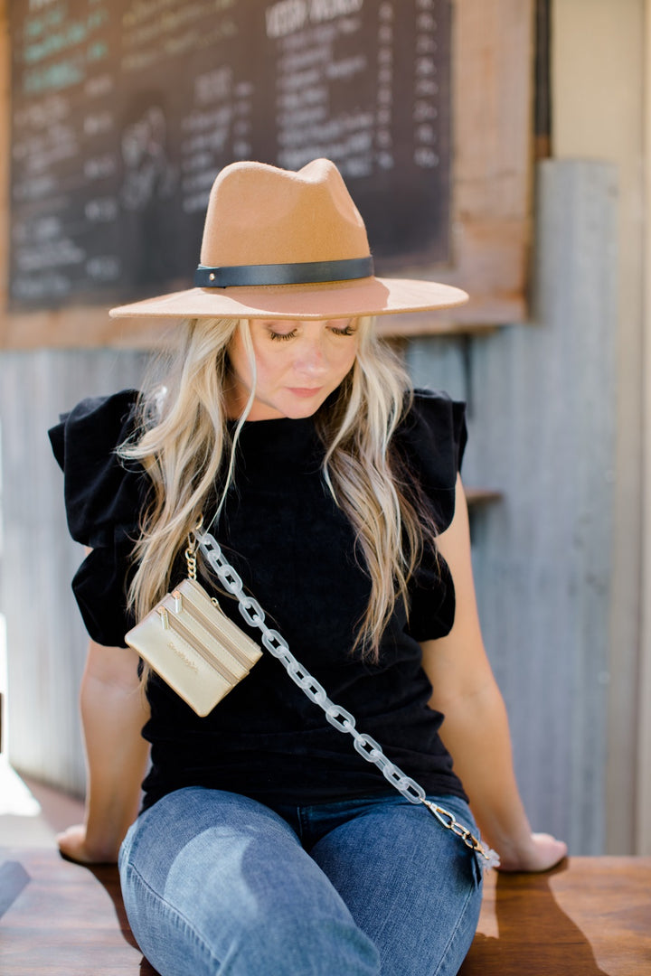 a woman wearing a black top and brown hat sitting outside wearing the white and gold clip and go chain