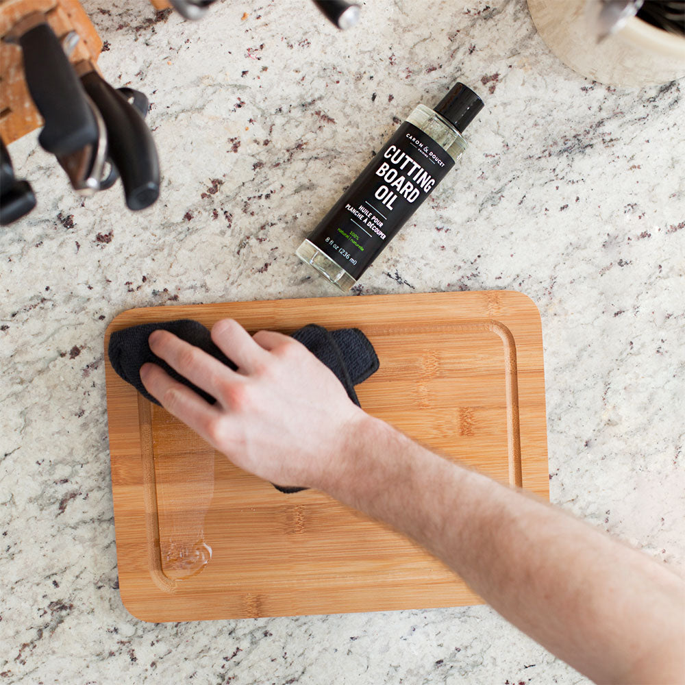 the cutting board conditioning oil being used on a cutting board on a marble countertop
