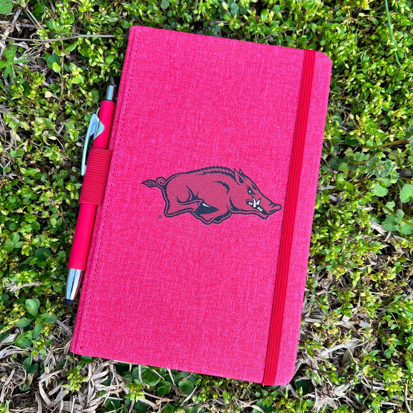 red journal with razorback logo in the center and red pen  and an elastic loop along the side to keep it closed.