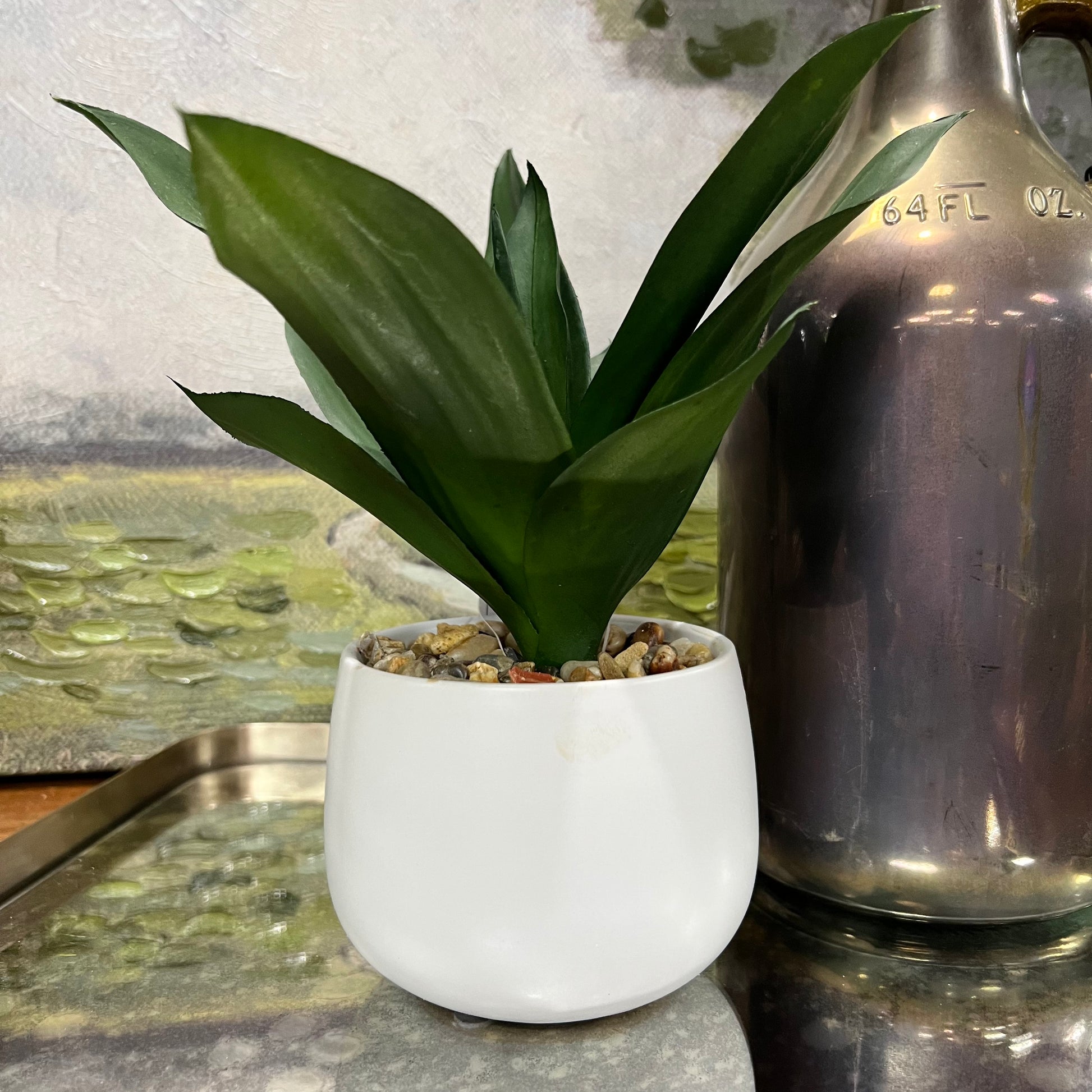 faux dark green plant in white pot on a table next to a vase.