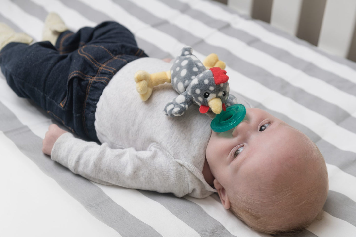 a baby laying in a crib on stiped sheets while suckling the rocky chicken pacifier