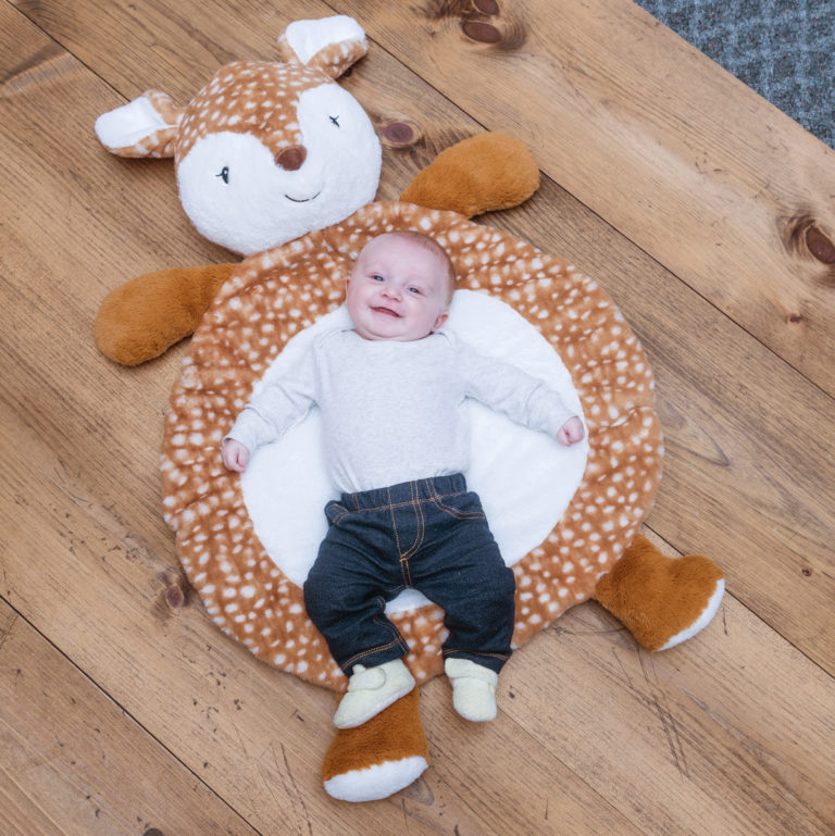 an infant boy laying on the amber fawn baby mat on a rustic wood floor