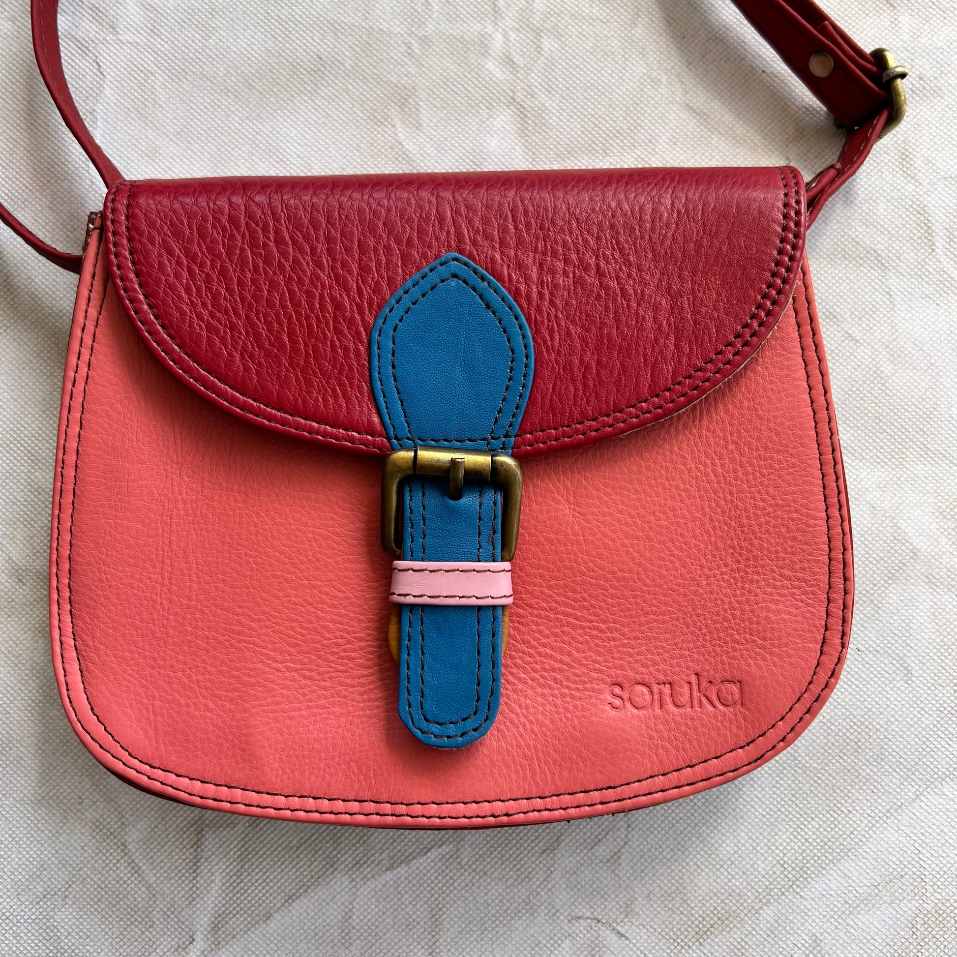 Rounded coral bag with red flap and blue buckle.