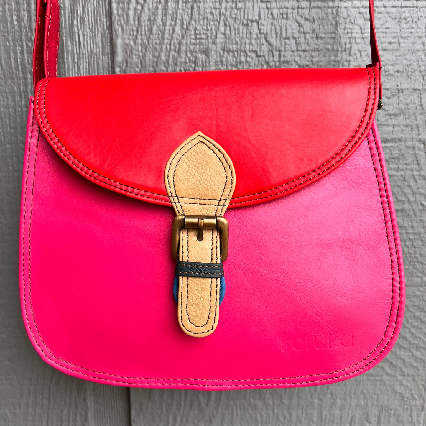 bright pink purse with red flap, yellow buckle, and red strap.