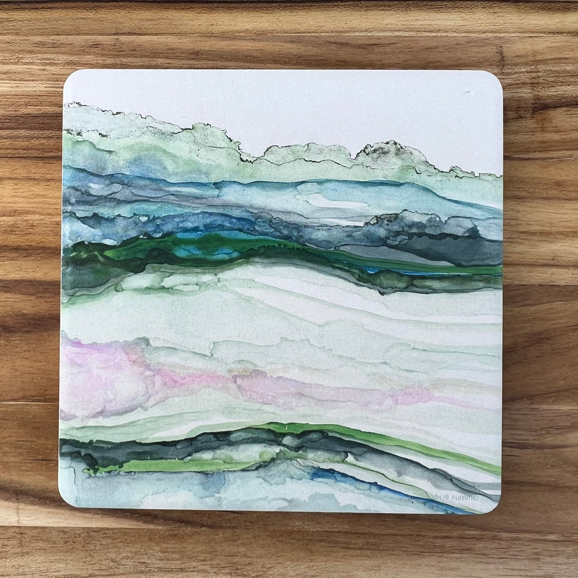 White stone coaster with abstract design of green hills.