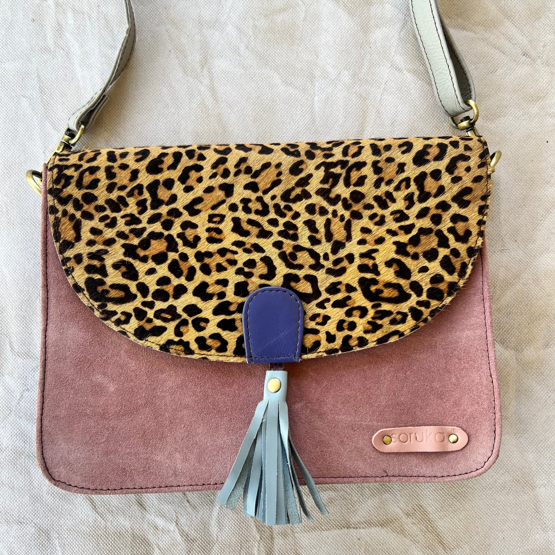 square pink bag with brown and black cheetah print flap, blue tassel, and grey strap.
