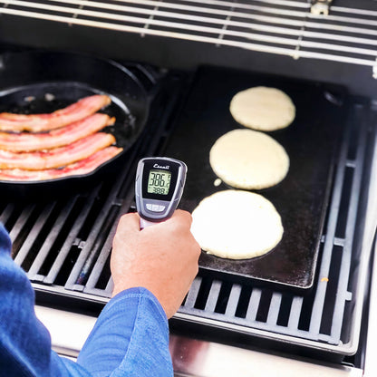 a persons hand holding the infrared surface and probe thermometer checking the temp of pancakes cooking on a grill