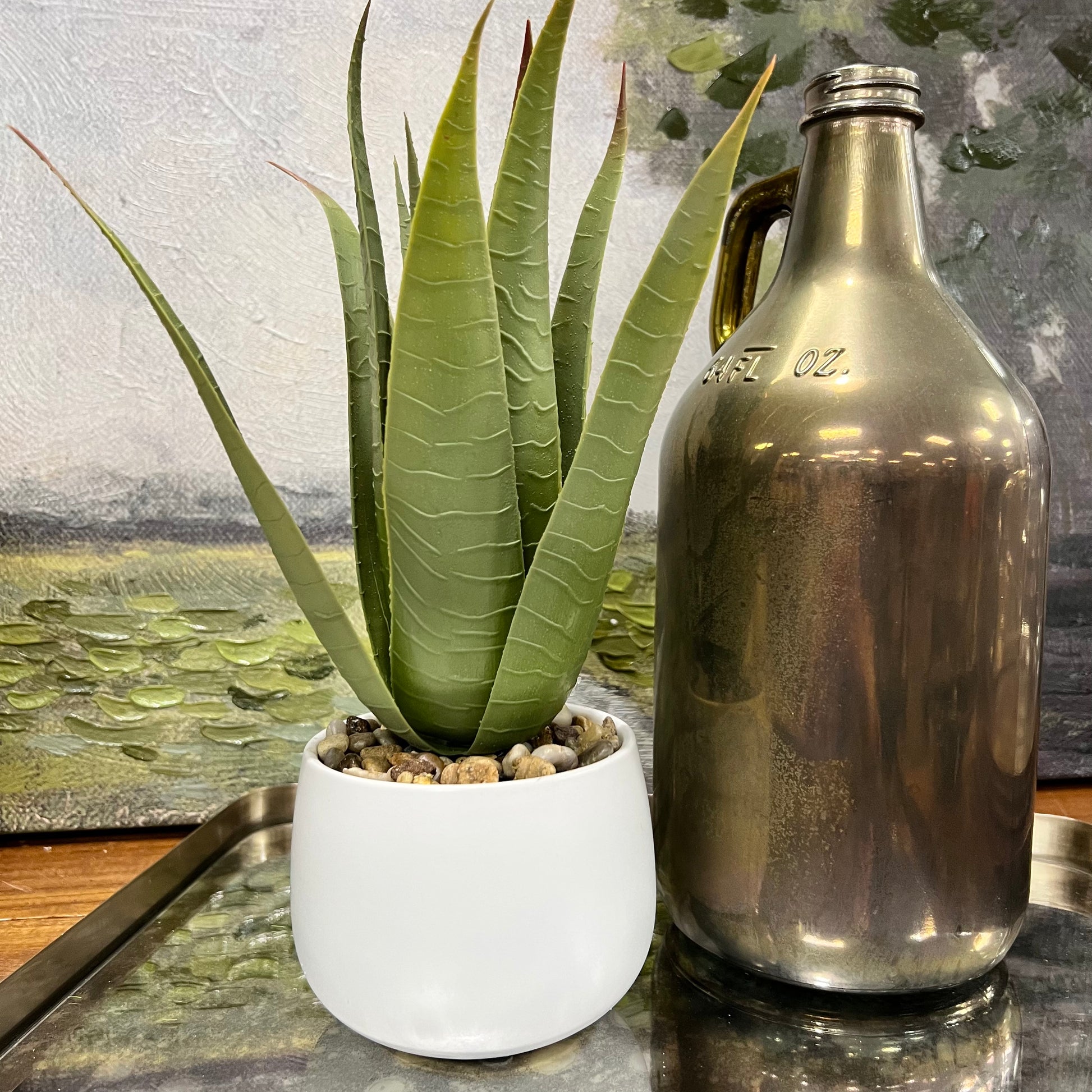 faux aloe plant in white pot on a table next to a vase.
