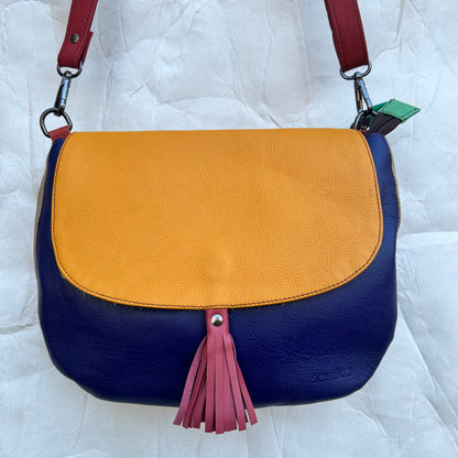 rounded blue purse with yellow flap, pink tassel, and red strap.