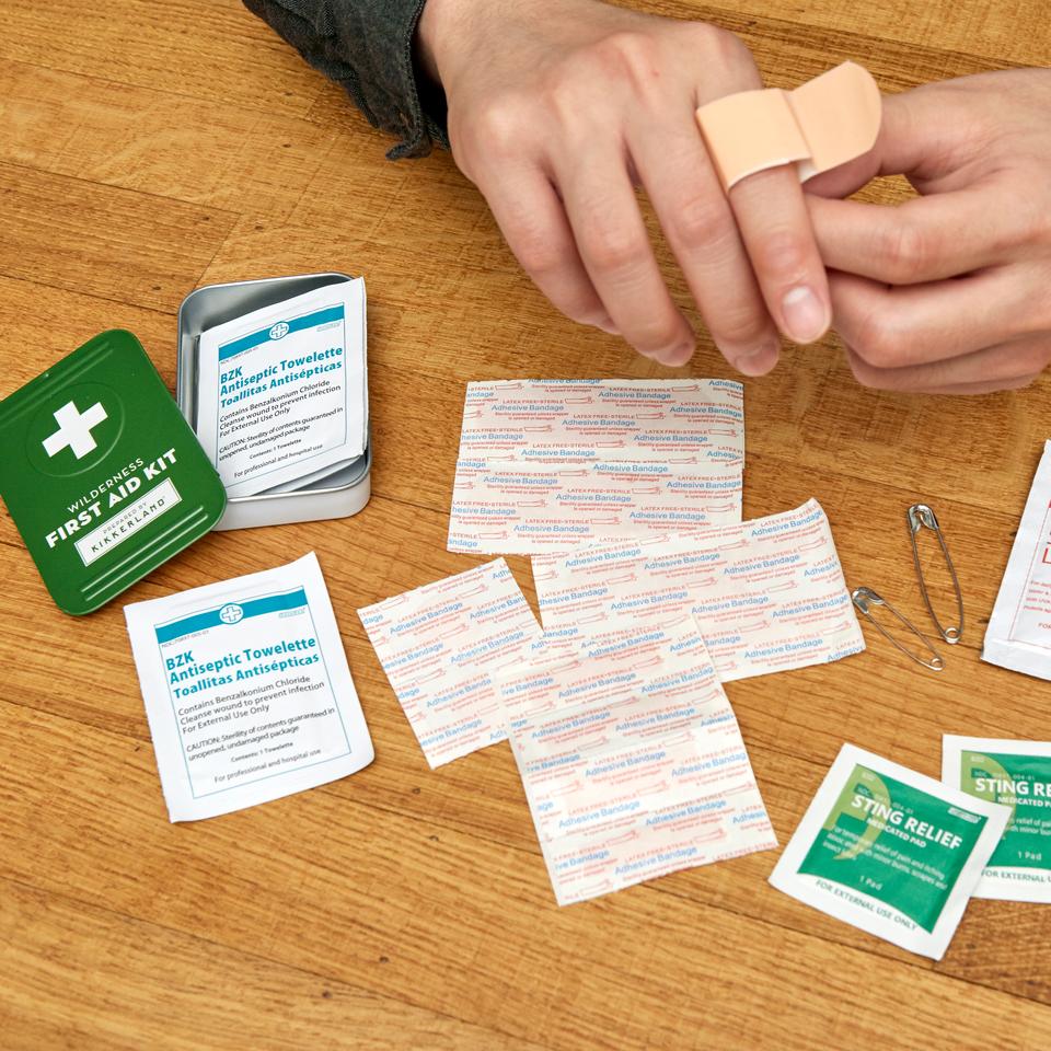 wilderness first aid kit displayed on a wood surface with a person applying a bandaid to their hand