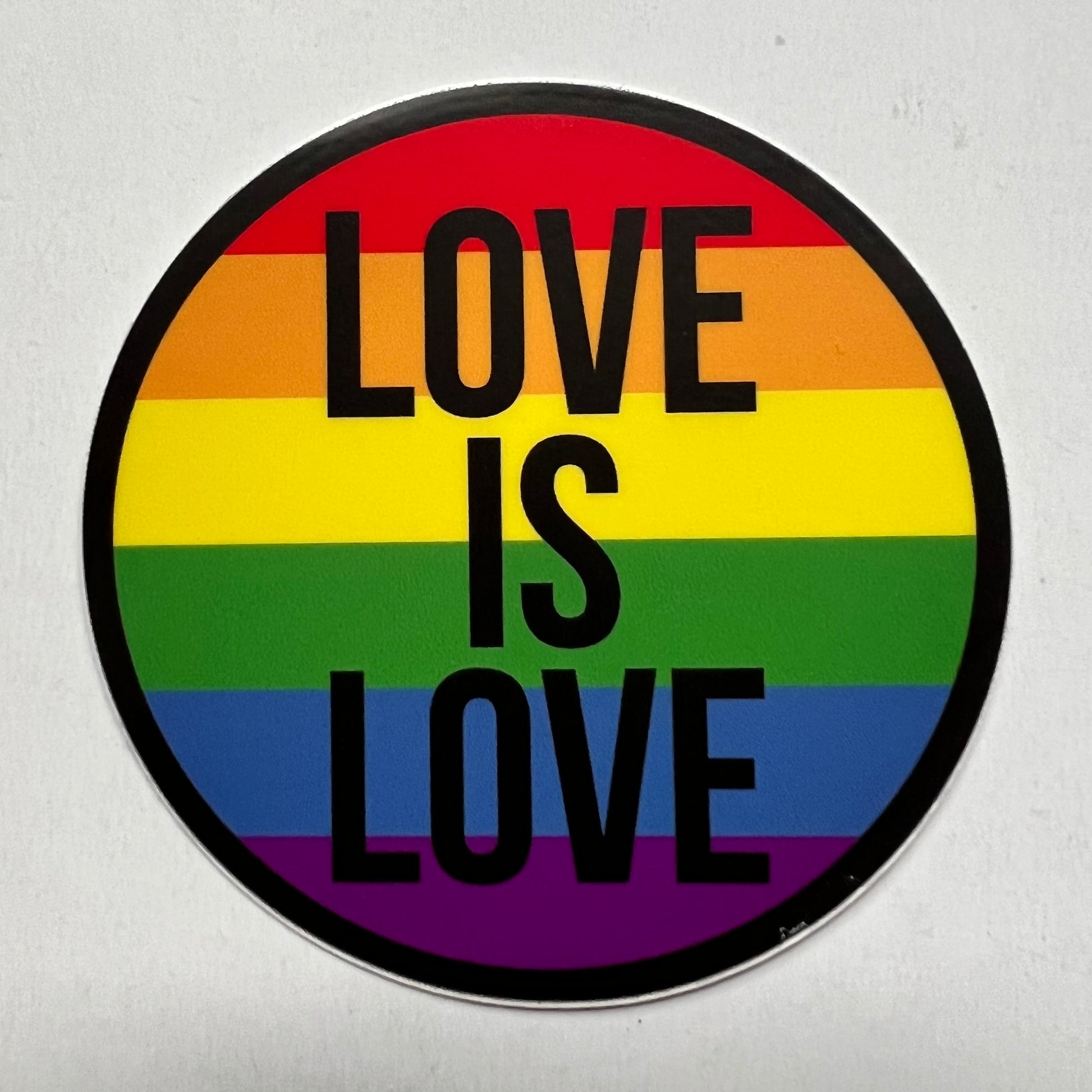 sticker on white background. round sticker has rainbow background with stacked words "love is love" in black.