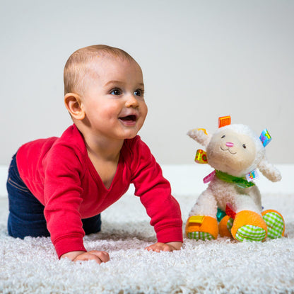 a baby girl crawling next to the sherbet lamb stuffed toy on a white rug