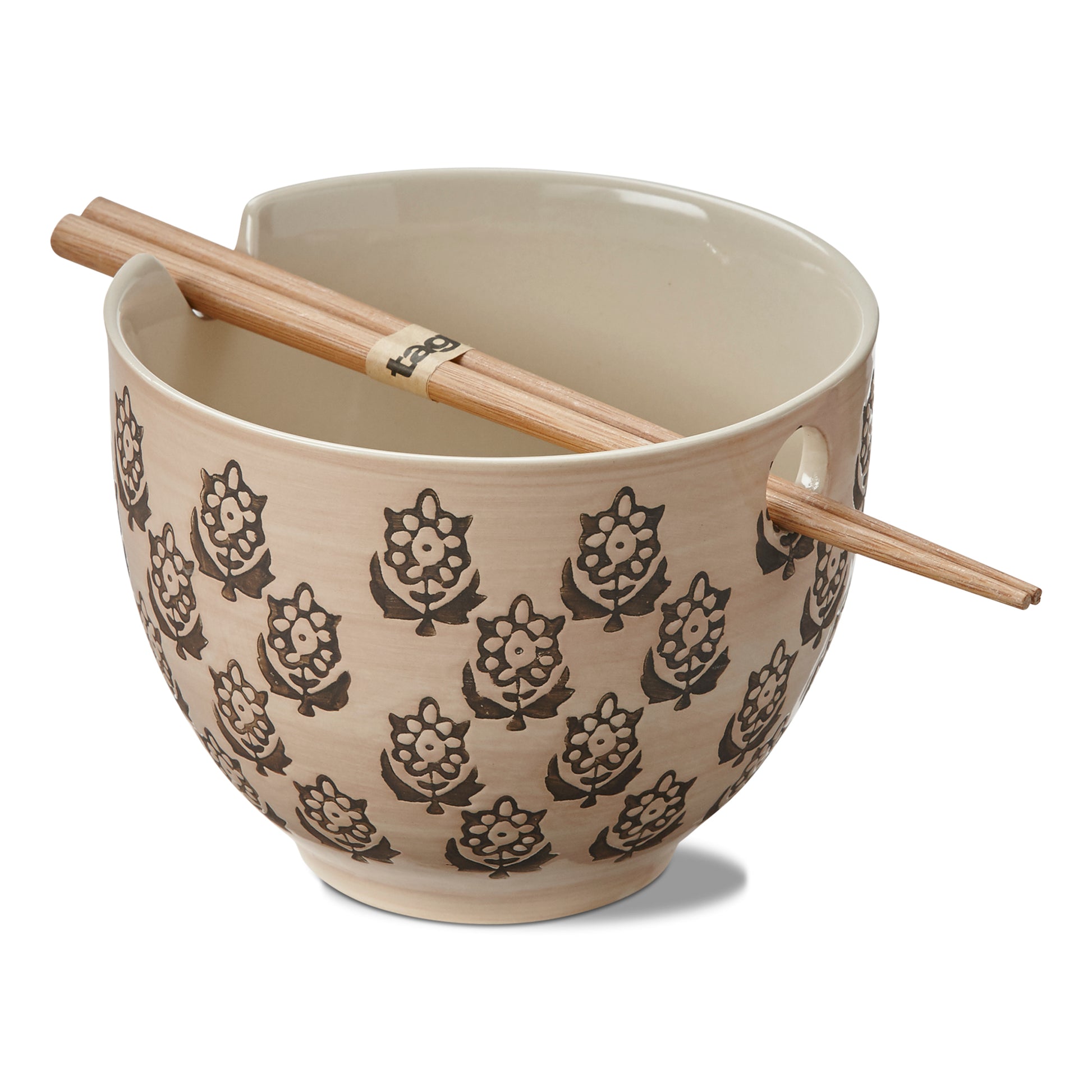 cream colored ceramic noddle bowl with flower design has chop sticks resting across the top on a white background.