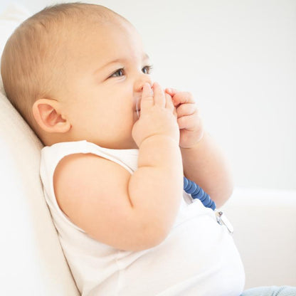 baby laying with a paci in mouth attached to the navy pacifier clip against a white background